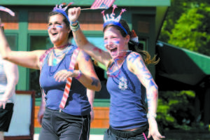 SHOWING THEIR PATRIOTIC SPIRIT — Camp Newfound counselors Izzy Perea and Claire Smith wave to spectators on Main Street during last Thursday's Bridgton 4 on the Fourth Road Race. (Rivet Photos)