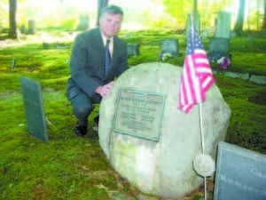 Steve Lyons kneels beside the gravestone of his great uncle, Captain Richard Mayberry, who was honored recently as a patriot who fought in the American Revolutionary War. (De Busk Photo) 