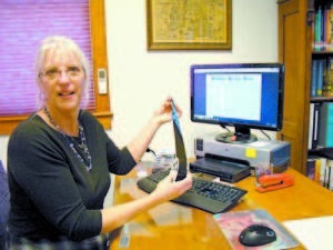 Holly Hancock, librarian at Bridgton Public Library, holds a reel of microfilm that is obsolete now that back issues of the Bridgton News are being digitally archived, as shown on her computer monitor.  