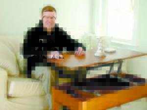 JUSTIN MCIVER shows off a fold-up coffee table inside the cottage, just one of many space-efficient aspects of living small. (Geraghty Photos) 