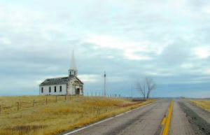 I LOVE THIS PICTURE â€” On his bookâ€™s website, Kevin Hancock writes of this church photograph, â€œI love this picture. I took it on the first day of my first trip to Pine Ridge. It captures so many elements of the Pine Ridge experience. Nature overshadows the human footprint. The church itself is symbolic of the effort to â€˜remakeâ€™ the Lakota, yet the church lies abandoned. The church, the road, the telephone poles are the only signs of human existence. From no vantage point can you see another building because it is a long way to the next one. When I took this picture, I just stopped my car in the road and got out. There was no traffic. Except for the wind, it was perfectly silent.â€