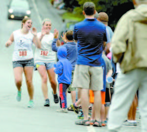 Sasha Azel (#103) and Yazi Azel (#102) of Lovell exchange high fives with youngsters standing near the Charlotte Hobbs Memorial Library during Saturday's Lovell Old Home Days 5K. (Rivet Photos)