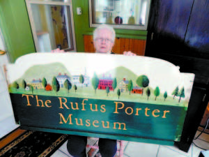  HOLDING UP JUST FINE â€” Artist Nelle Ely shows the hand-painted Rufus Porter Museum sign she created 11 years ago. Museum volunteers recently asked her to retouch the sign, and she repainted the gold lettering and the red houses. All the other paint held up very well, with minimal fading, said Ely. The sign was also sprayed with a car finish by Dale McDaniel, owner of Portland Street Auto. This finish, which McDaniel also applied to the municipal signs, makes the colors really â€œpop,â€ she said. Rufus Porter Museum Board member Beth Cossey said the museum is â€œso very grateful to both of them for their generous donations.â€   (Gail Geraghty Photo)